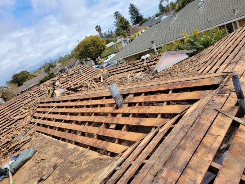 Roof under repair with exposed wooden rafters and scattered debris after storm damage