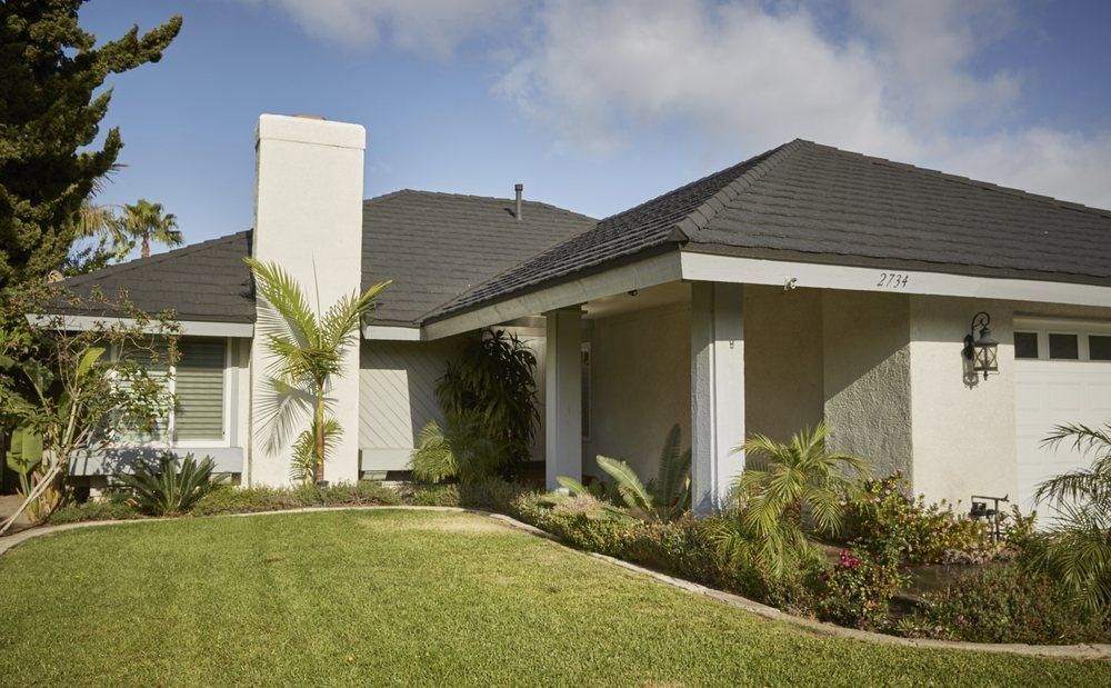 Modern single-story house with gray roof, white walls, chimney, and a green front lawn.