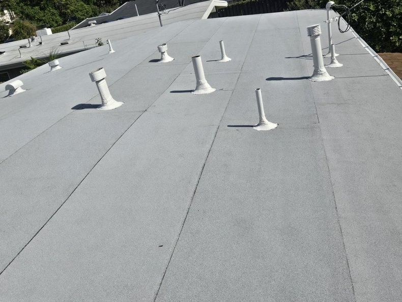 Gray flat rooftop with several white vent pipes and ducts under a blue sky