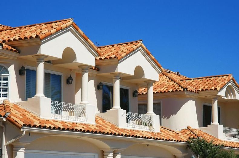 Spanish-style stucco homes with red tile roofs and white balconies against a blue sky