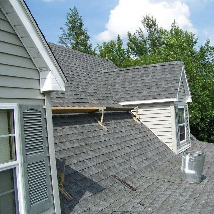 Roof repair with exposed wood and missing shingles on a gray house roof