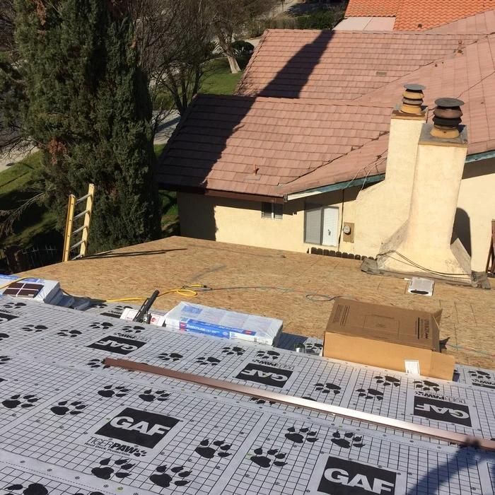 Roof under repair with GAF underlayment and cardboard boxes beside a house chimney