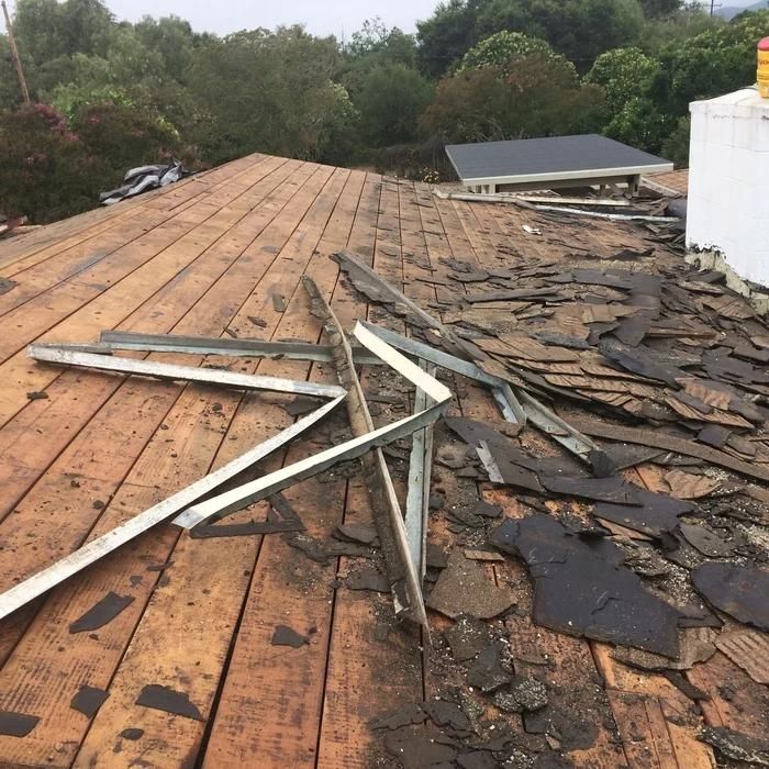 Rooftop with severe storm damage, broken white metal beams, and missing shingles