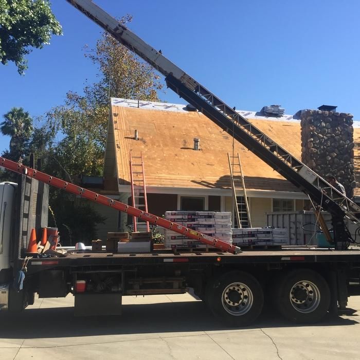 Construction crane truck lifting materials beside a partially wood-sided building under a clear blue sky