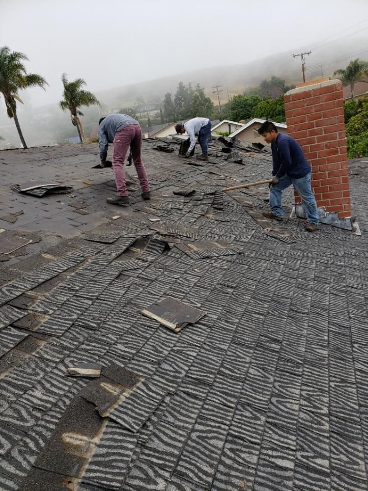 Workers repairing a damaged shingled roof in foggy weather