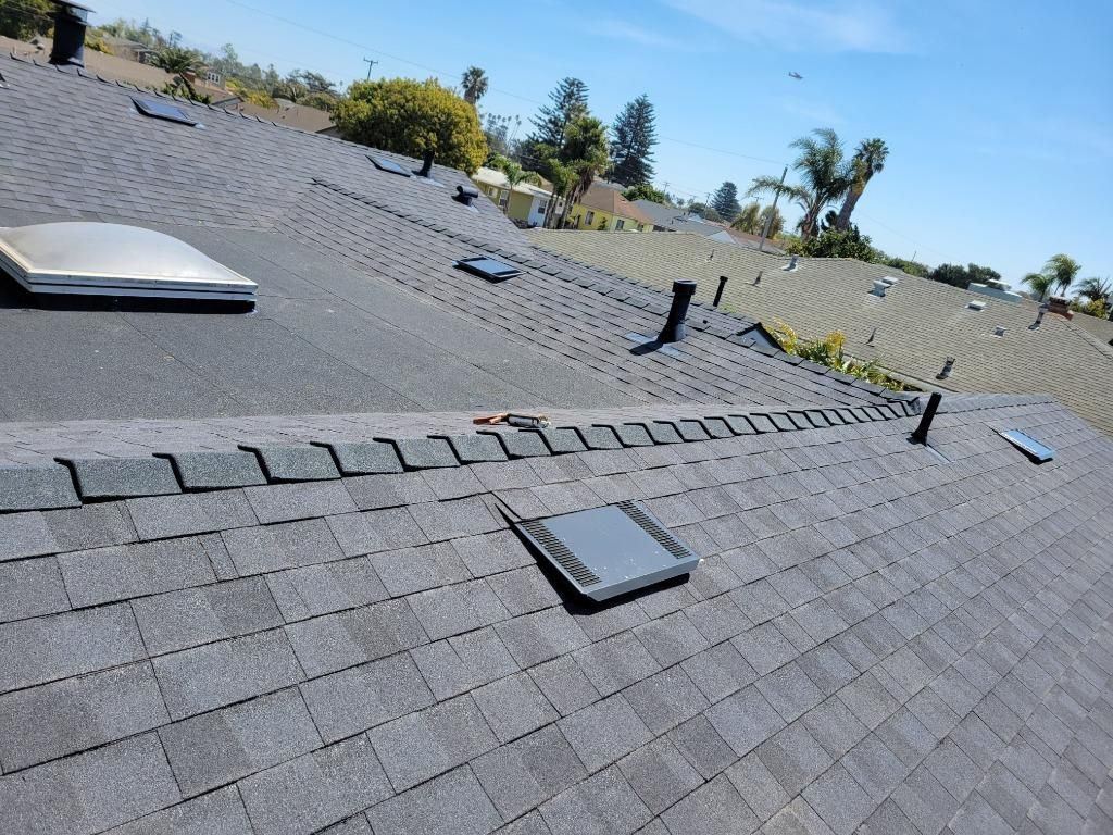 Flat shingle rooftop with vents and skylights under a clear blue sky