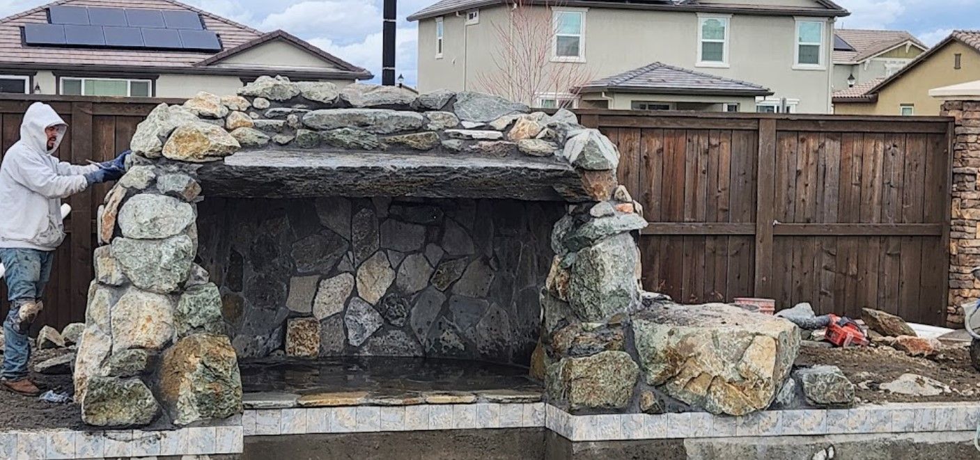 A man is working on a stone fireplace in a backyard.