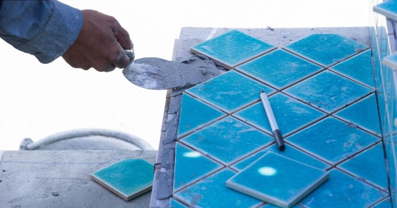 A man is laying blue tiles on a table with a trowel.