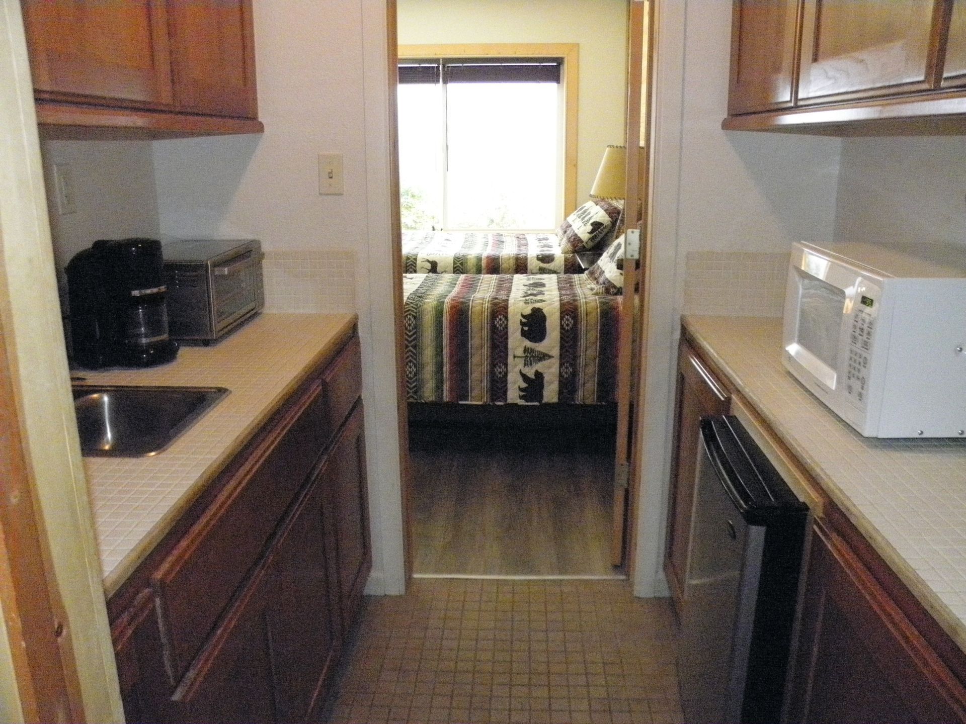 A kitchen with a microwave and a sink leading to a bedroom