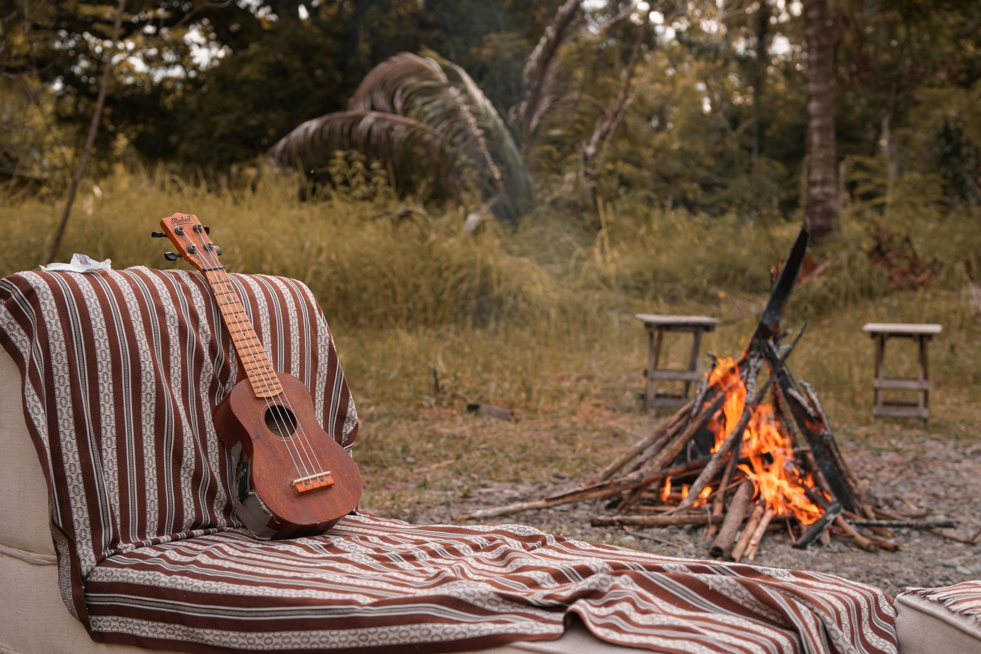 A guitar is sitting on a blanket next to a campfire.