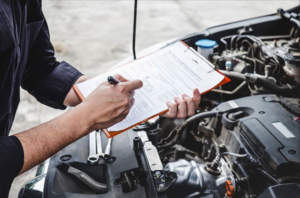 A mechanic is writing on a clipboard while working on a car.
