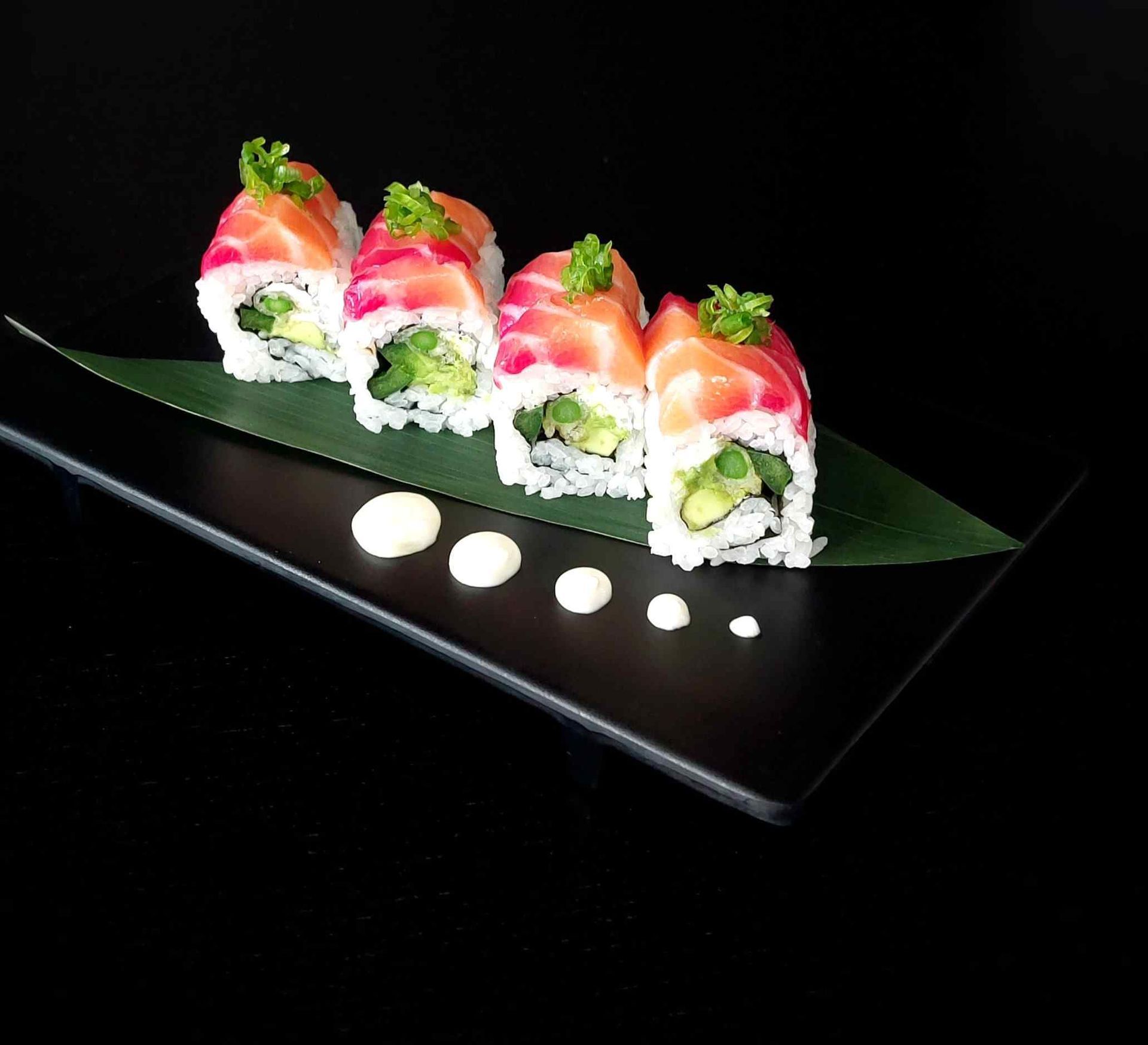 A black plate topped with sushi on a green leaf