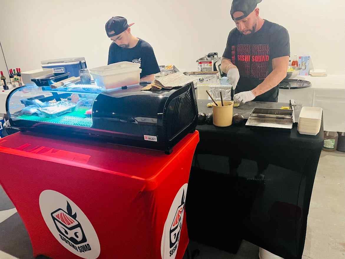 Two sushi chefs are working in a kitchen preparing food.