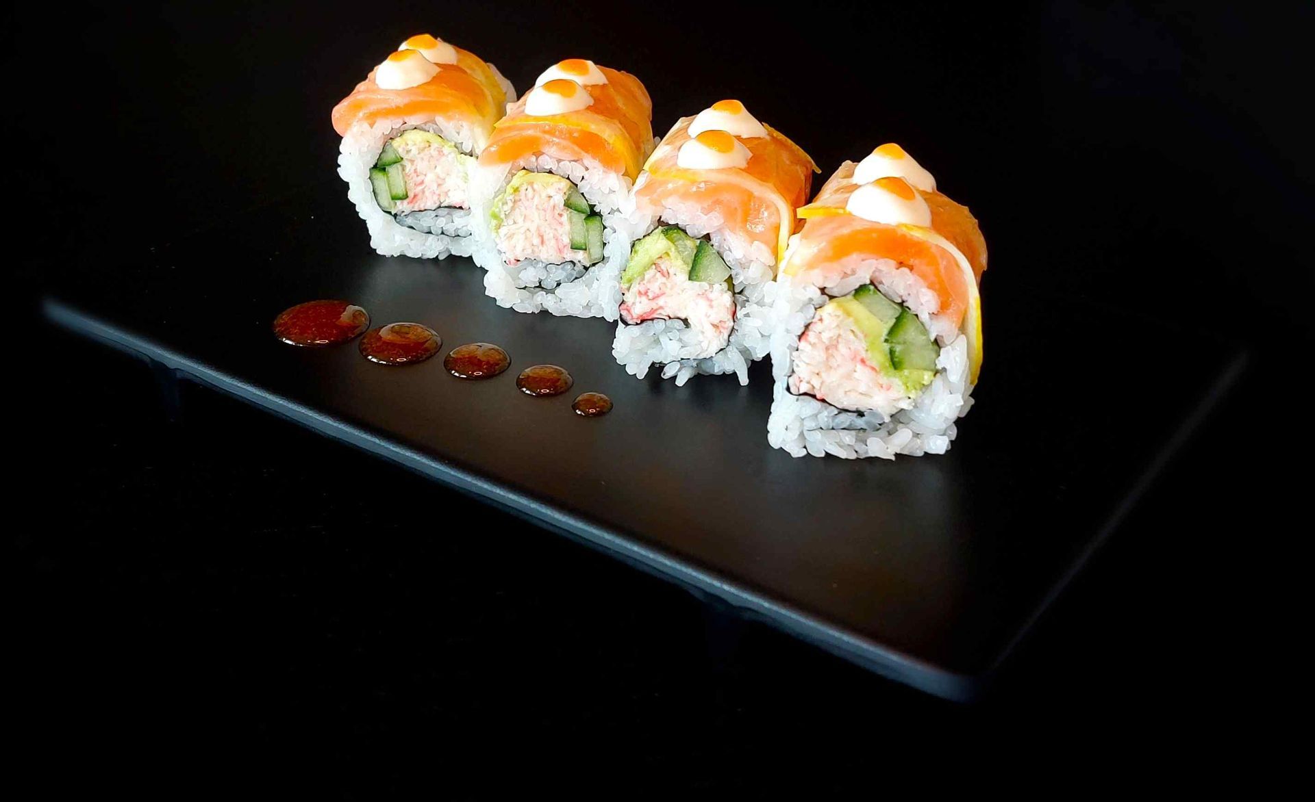 A black plate topped with sushi rolls and sauce on a black background.