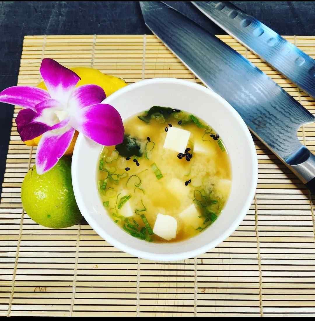 A bowl of soup with a purple flower in it