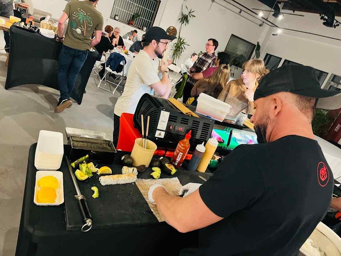 A sushi chef is cooking food at a table in front of a crowd of people.