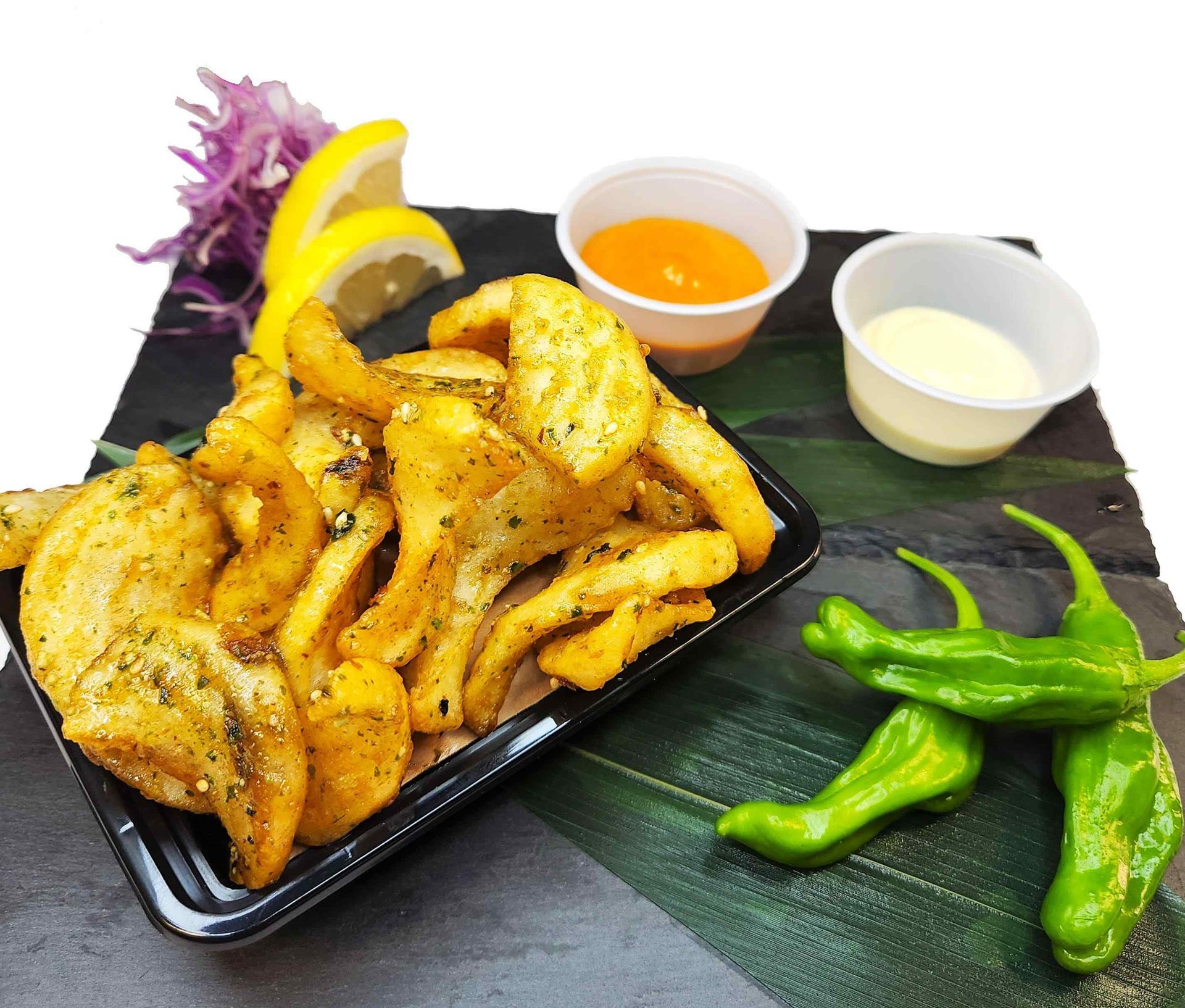 A plate of french fries with dipping sauces and green peppers on a table.