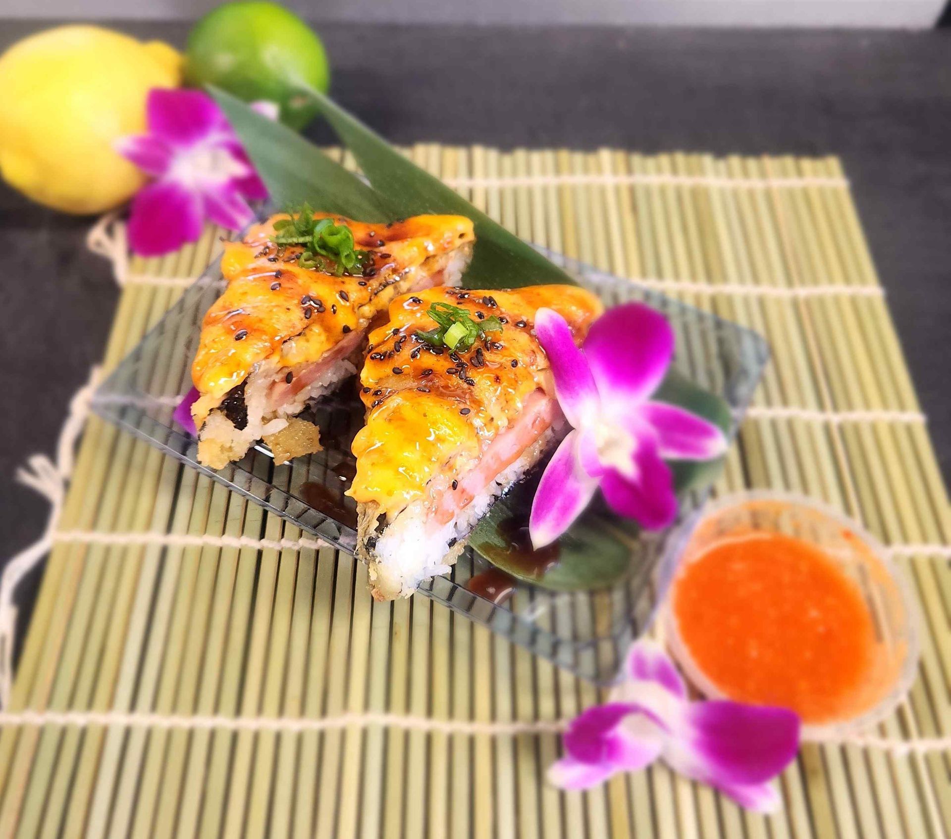 A plate of sushi with flowers and sauce on a bamboo mat.