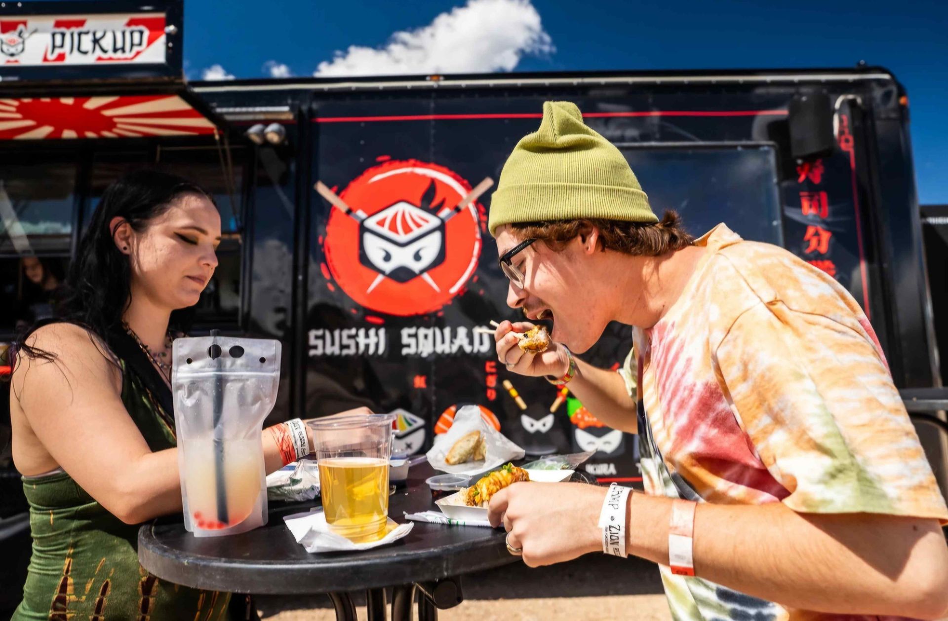 A man and a woman are sitting at a table eating food from a sushi truck.