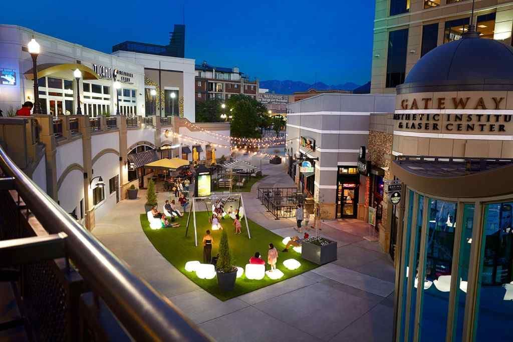 An aerial view of a shopping mall at night with people sitting on the grass.