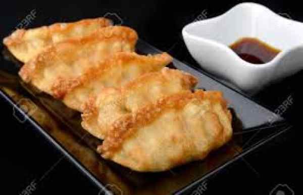 A black plate topped with fried dumplings next to a bowl of dipping sauce.
