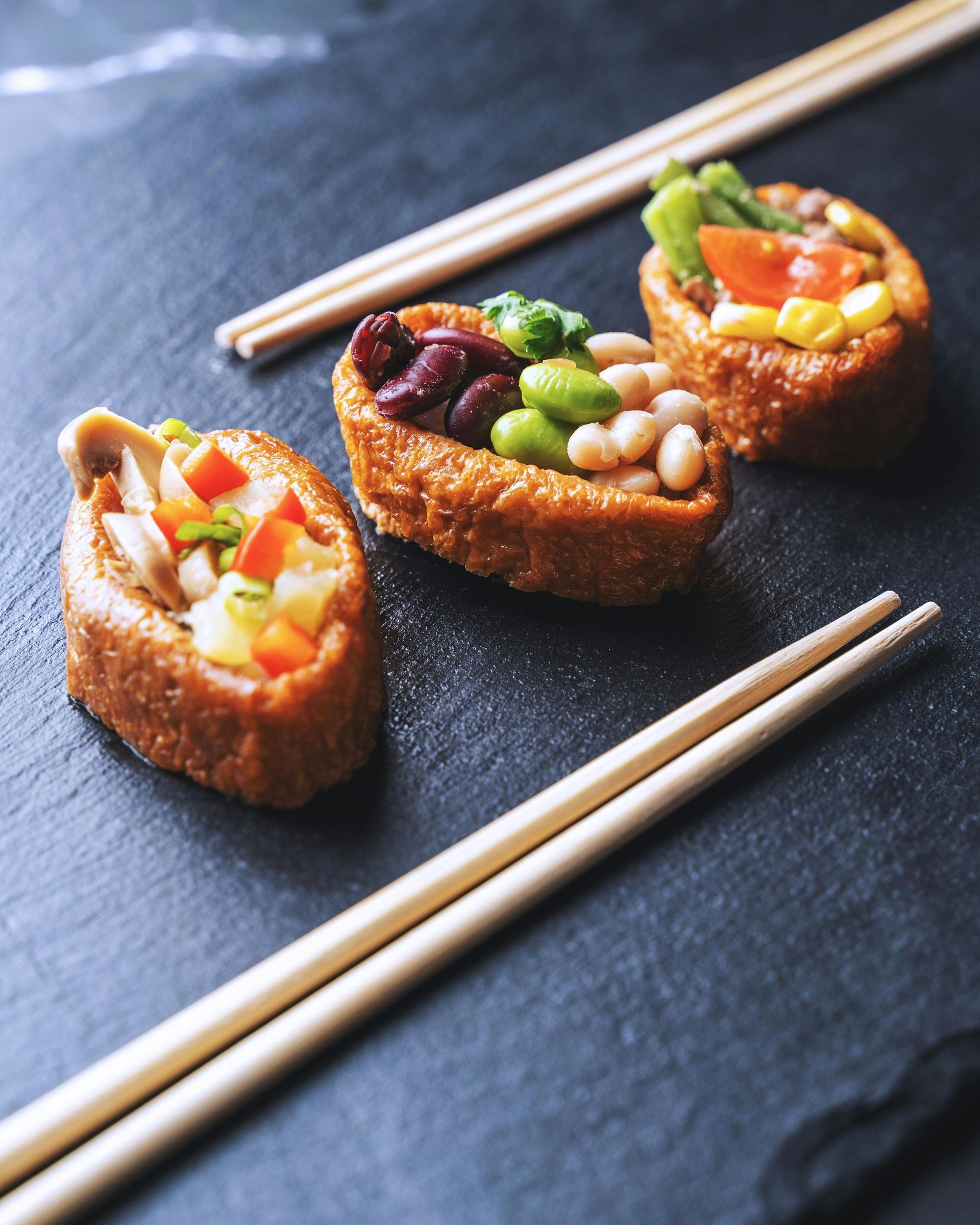 Three pieces of sushi with chopsticks on a black surface
