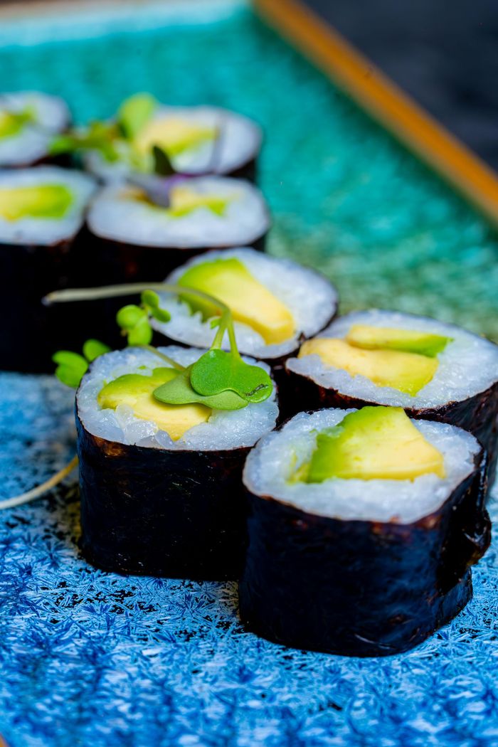 A close up of sushi rolls with avocado on a blue plate.