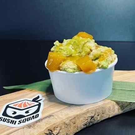 A bowl of guacamole with mango sauce on a wooden cutting board.