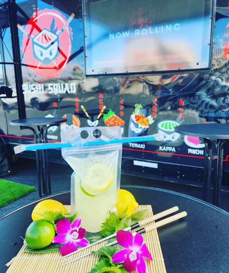 A glass of lemonade sits on a table in front of a sushi truck