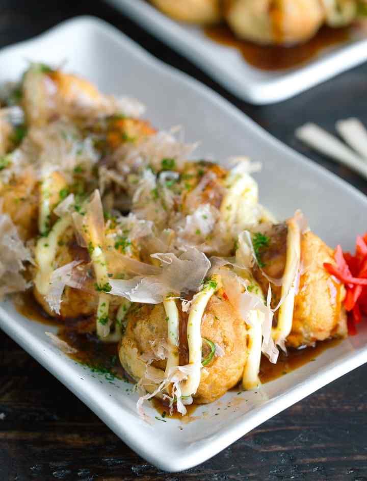 A white plate topped with takoyaki and sauce on a table.