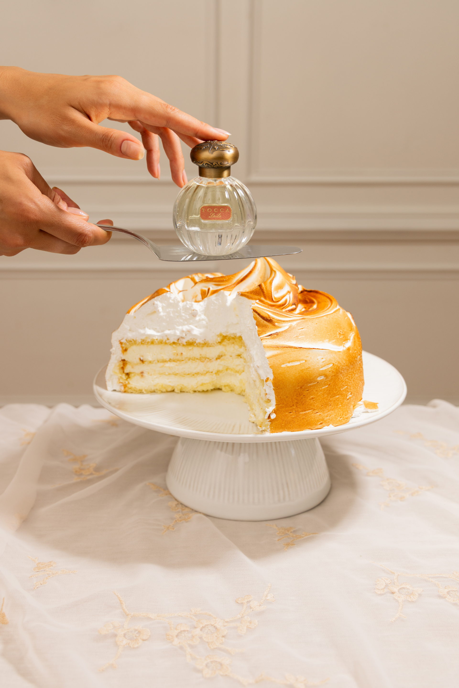 A sliced lemon meringue cake on a white cake stand, next to a perfume bottle.