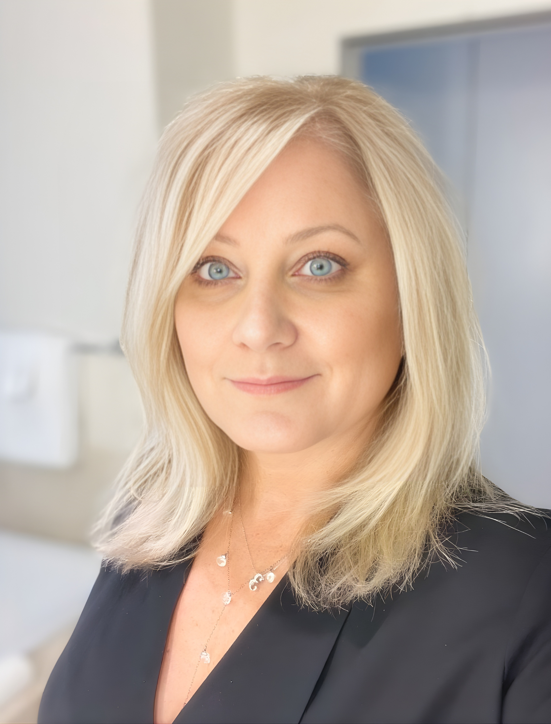 Woman with blonde hair, blue eyes, wearing black top, looking at camera.