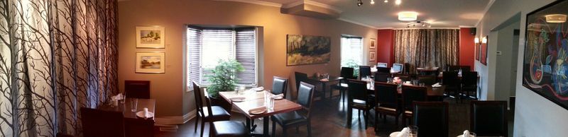 Restaurant interior with tables, chairs, windows, artwork, and decorative curtains.