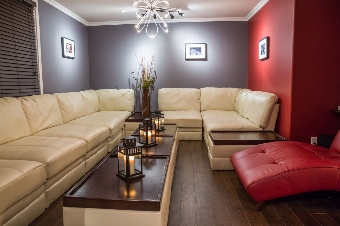 A modern living room with cream sectional sofa, red accent wall, dark wood floors, and a chaise lounge.
