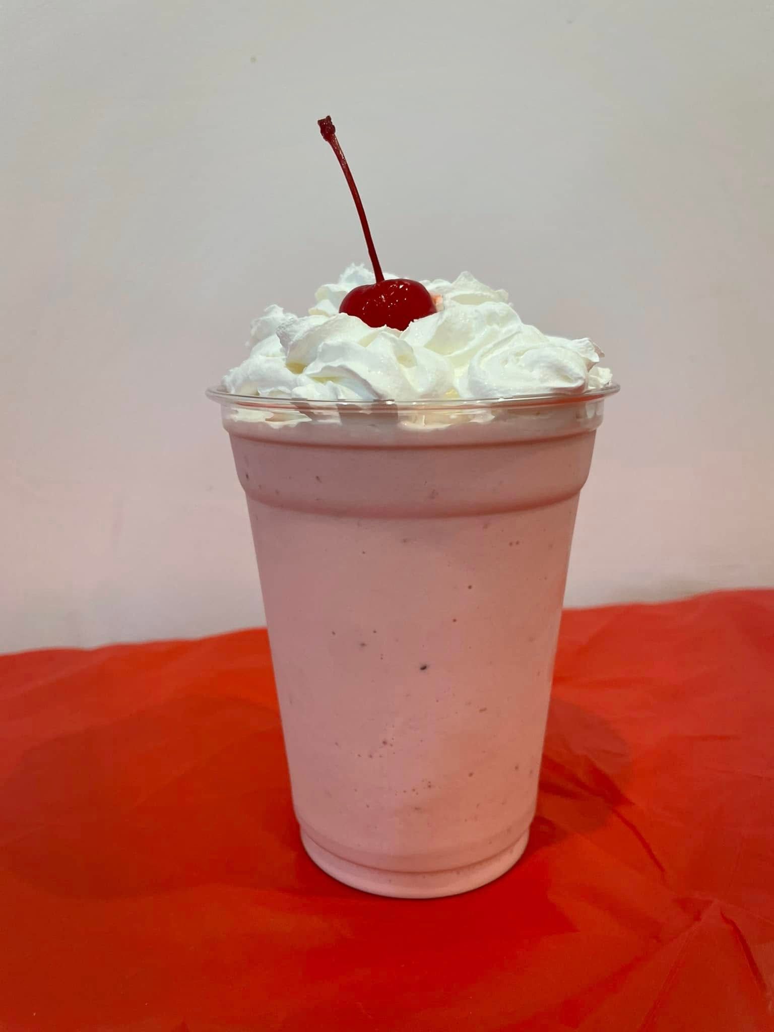 A milkshake with whipped cream and a cherry on top is on a red table.