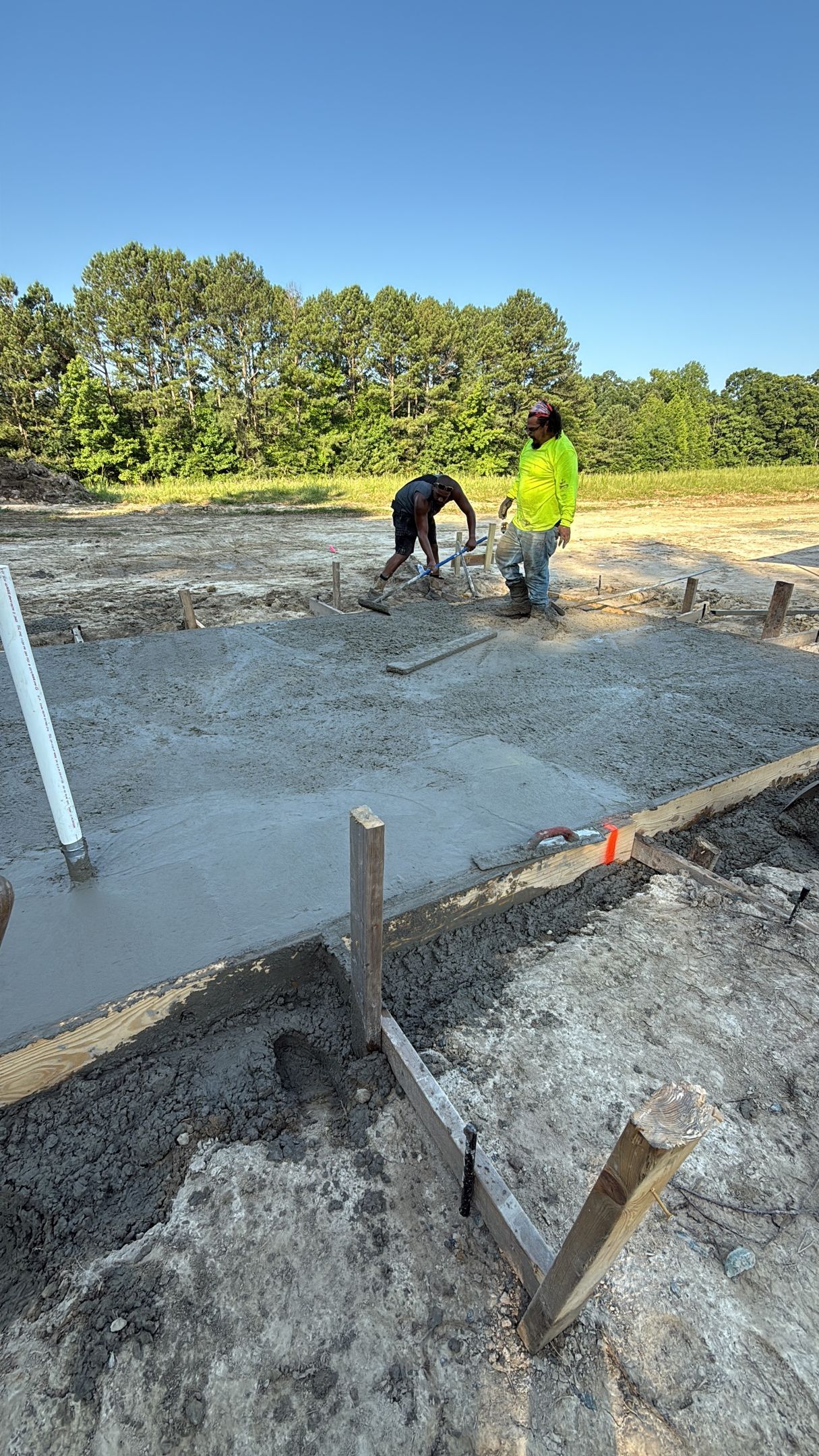 Person smoothing wet concrete with a power screed in a construction setting.