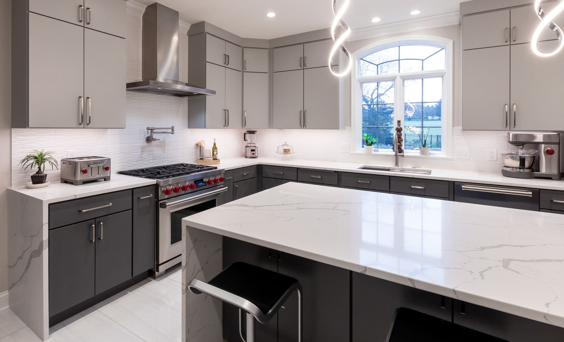 A kitchen with gray cabinets , white counter tops , stainless steel appliances and a large island.