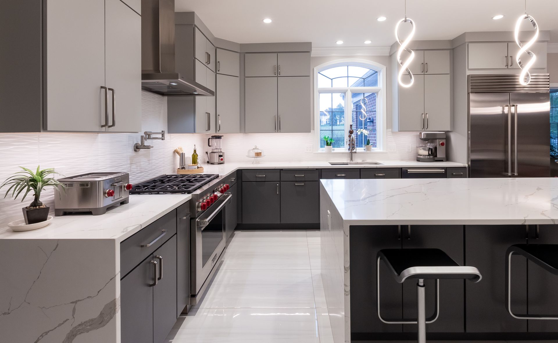 A kitchen with gray cabinets , white counter tops , stainless steel appliances and a large island.