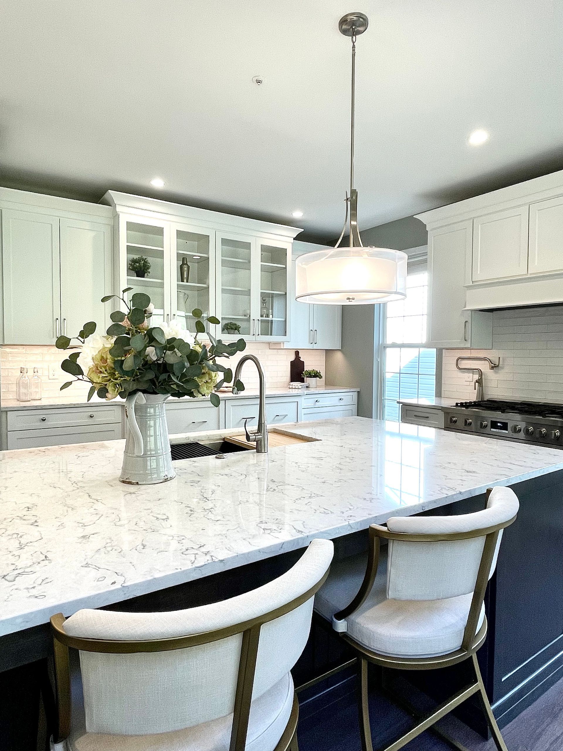 A kitchen with a large island , chairs , a sink and a stove.
