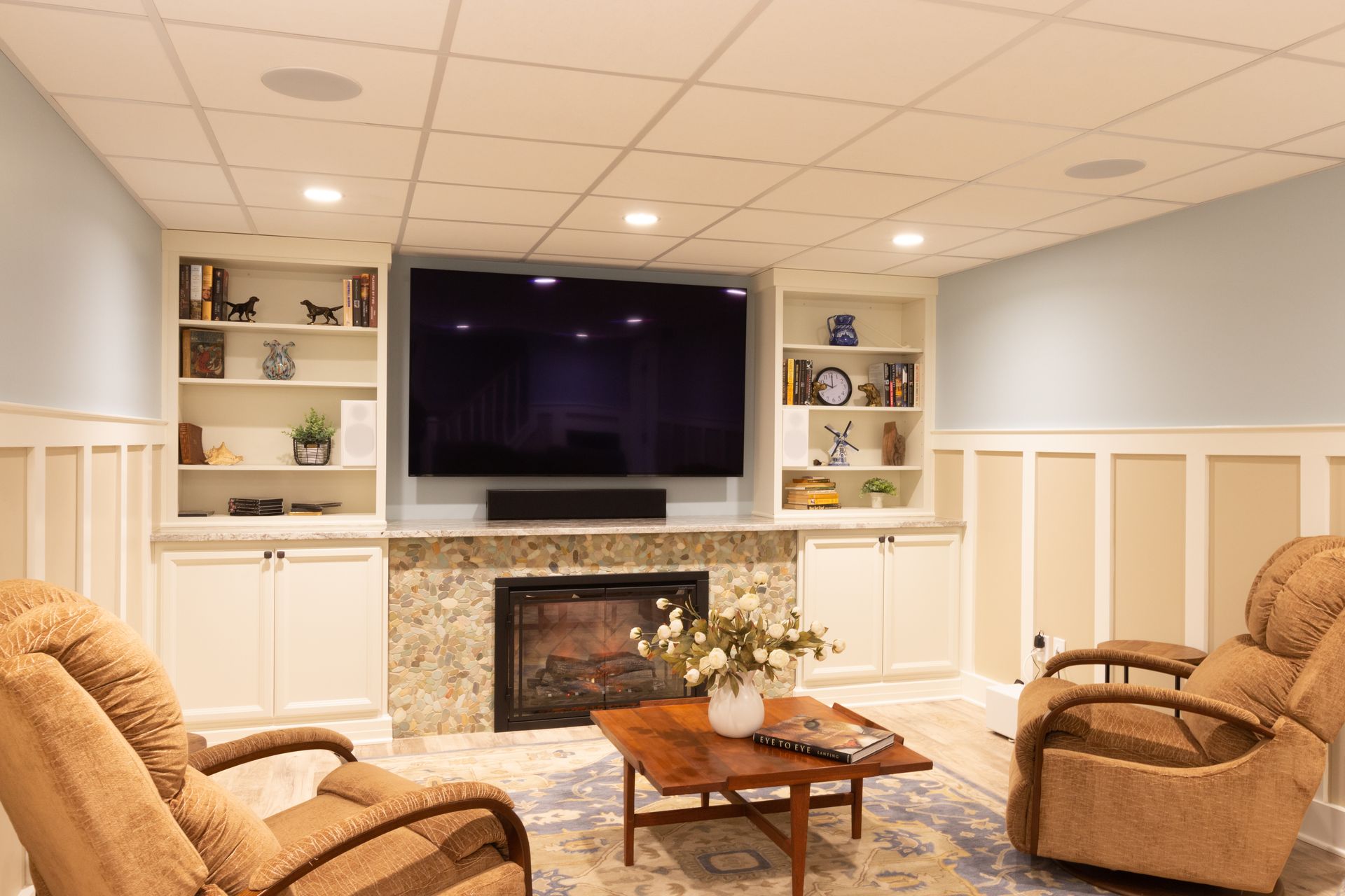 A living room with two recliner chairs , a fireplace , a flat screen tv and a coffee table.