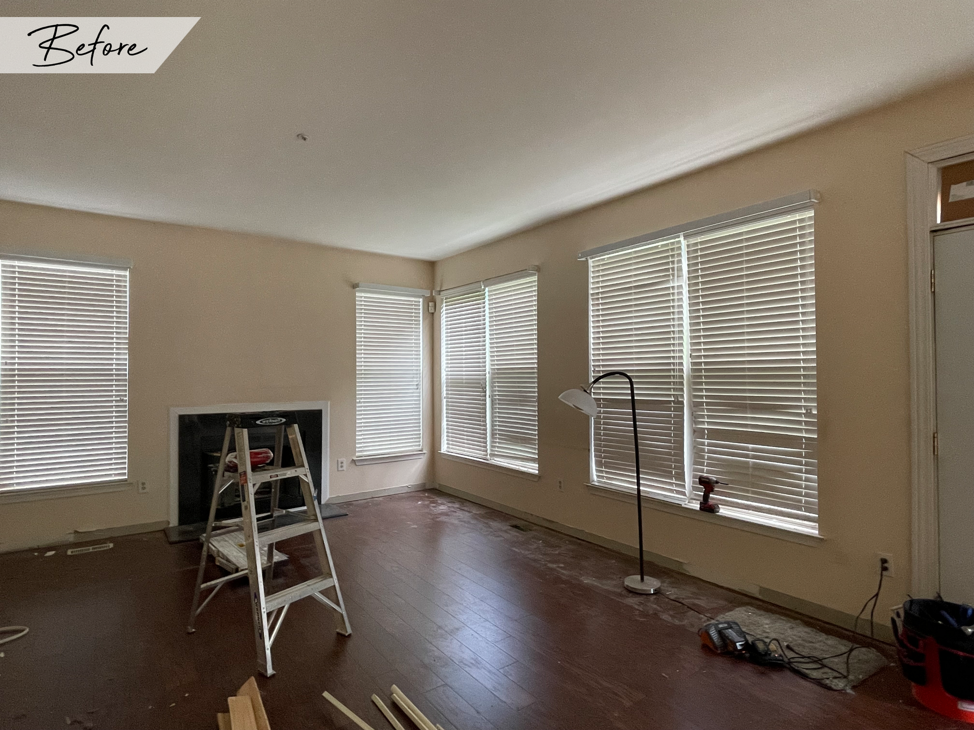 A before picture of a living room with a fireplace and blinds