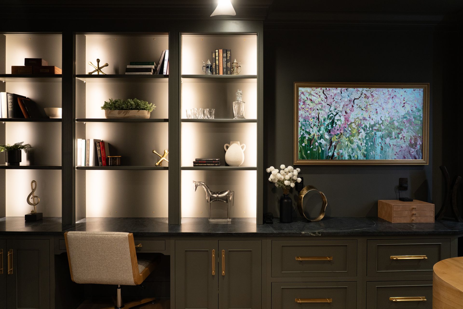 A living room with a desk , chair , shelves and a television.