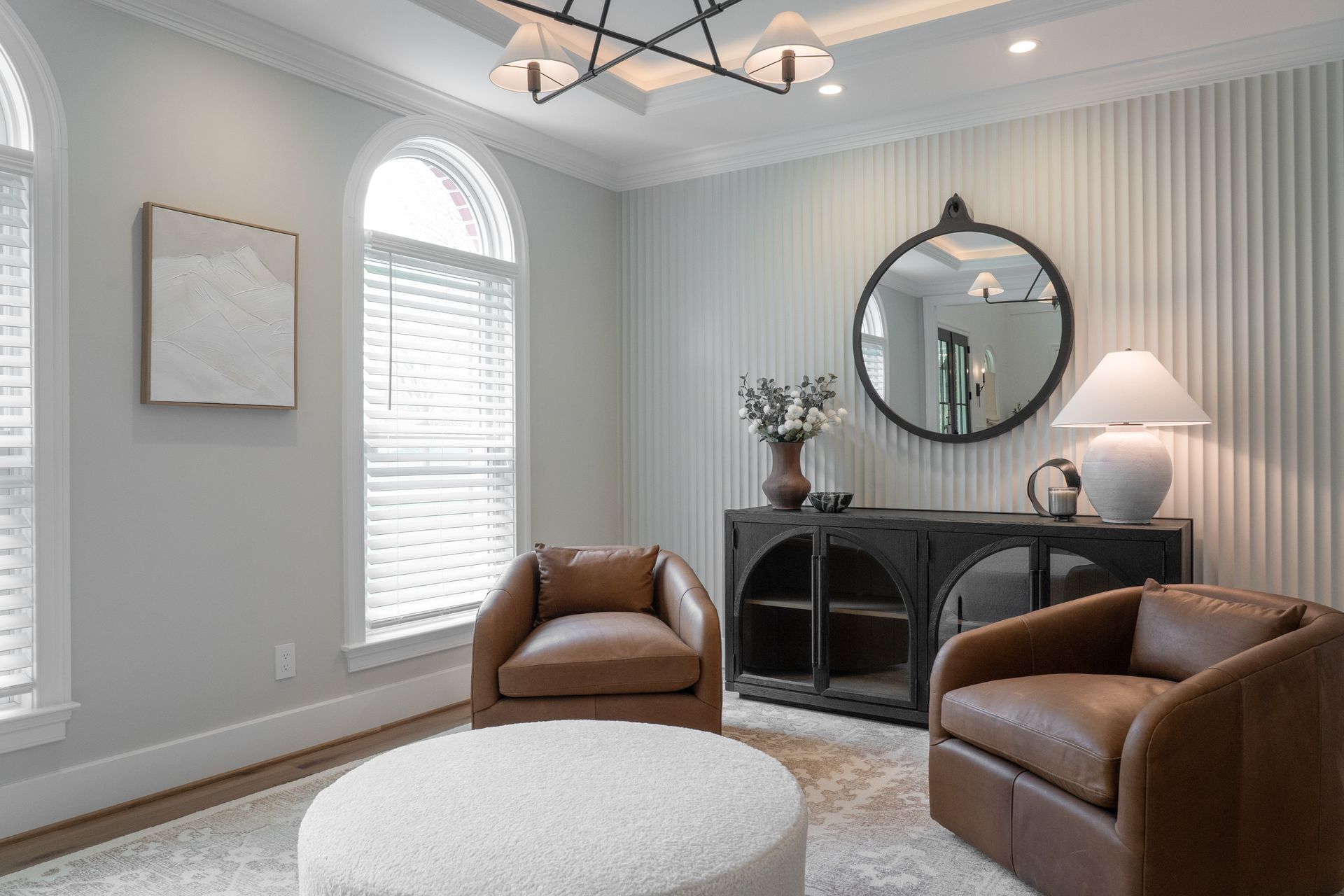 A living room with two chairs , an ottoman , and a mirror.