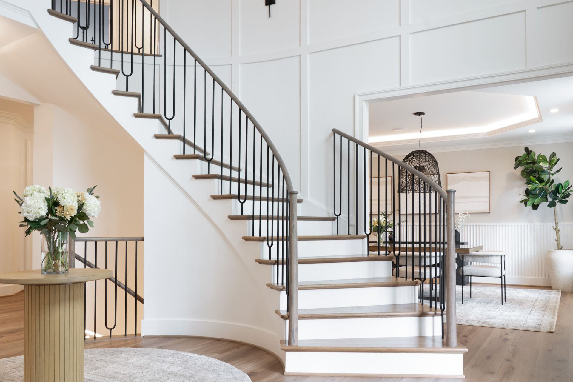 A curved staircase in a house with a vase of flowers on a table.