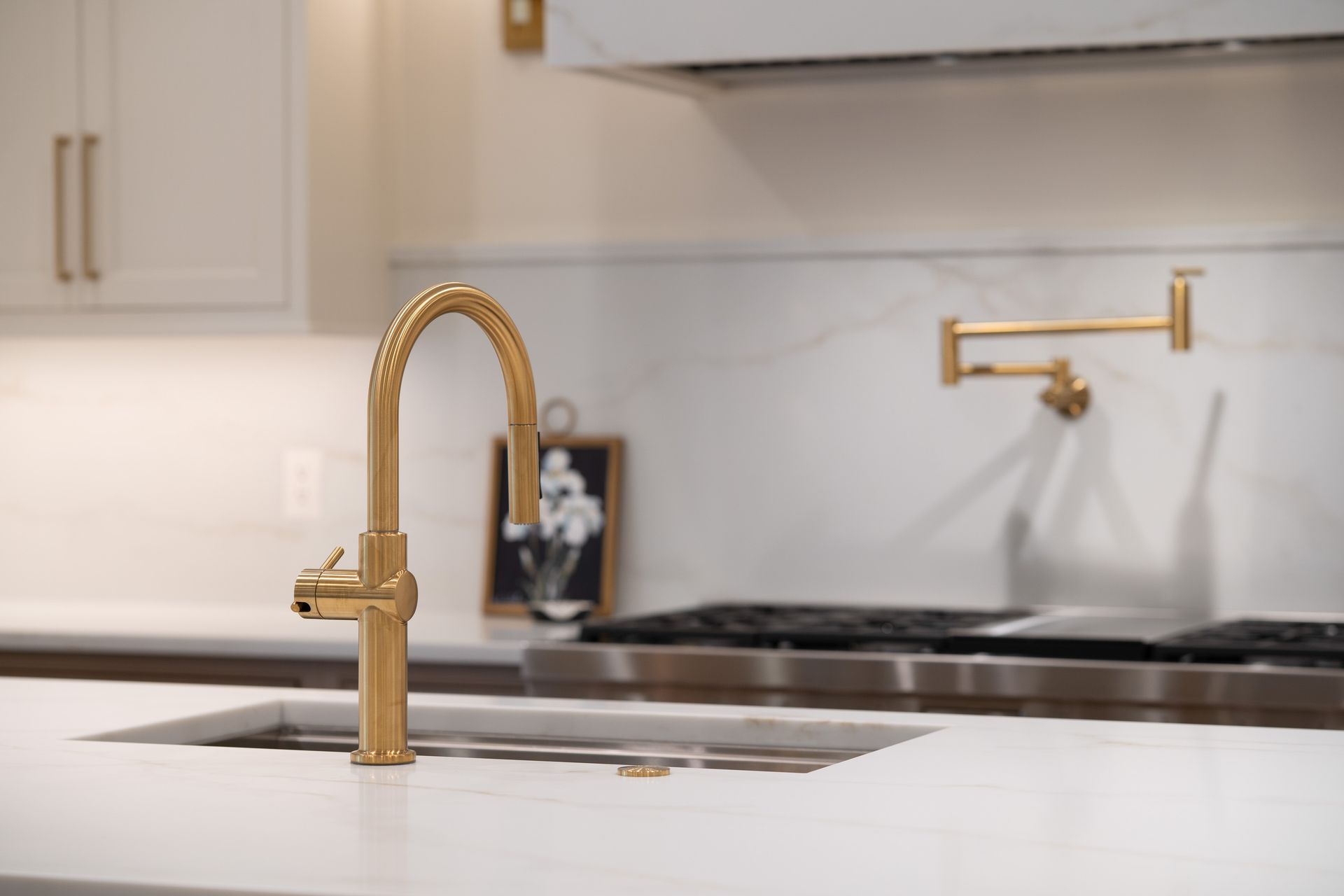 A kitchen sink with a gold faucet and a stove in the background.