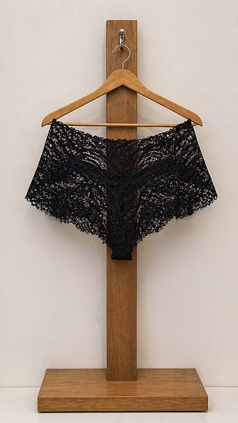Pantalones cortos de encaje negro en una percha de madera contra una pared lisa, colgados en un soporte de madera.