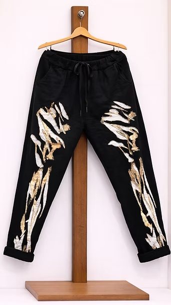 Pantalones deportivos negros con estampados beige que simulan llamas, colgados en un soporte de madera.