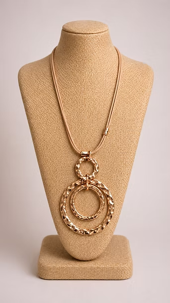 Collar de cadena de oro con colgante circular expuesto en un soporte de joyería color beige.