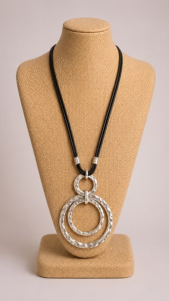 Collar de cordón negro con colgante de doble anillo plateado exhibido en un busto de maniquí beige.