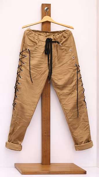 Pantalones cargo color canela colgados en un soporte de madera, con puños enrollados y cordones negros.